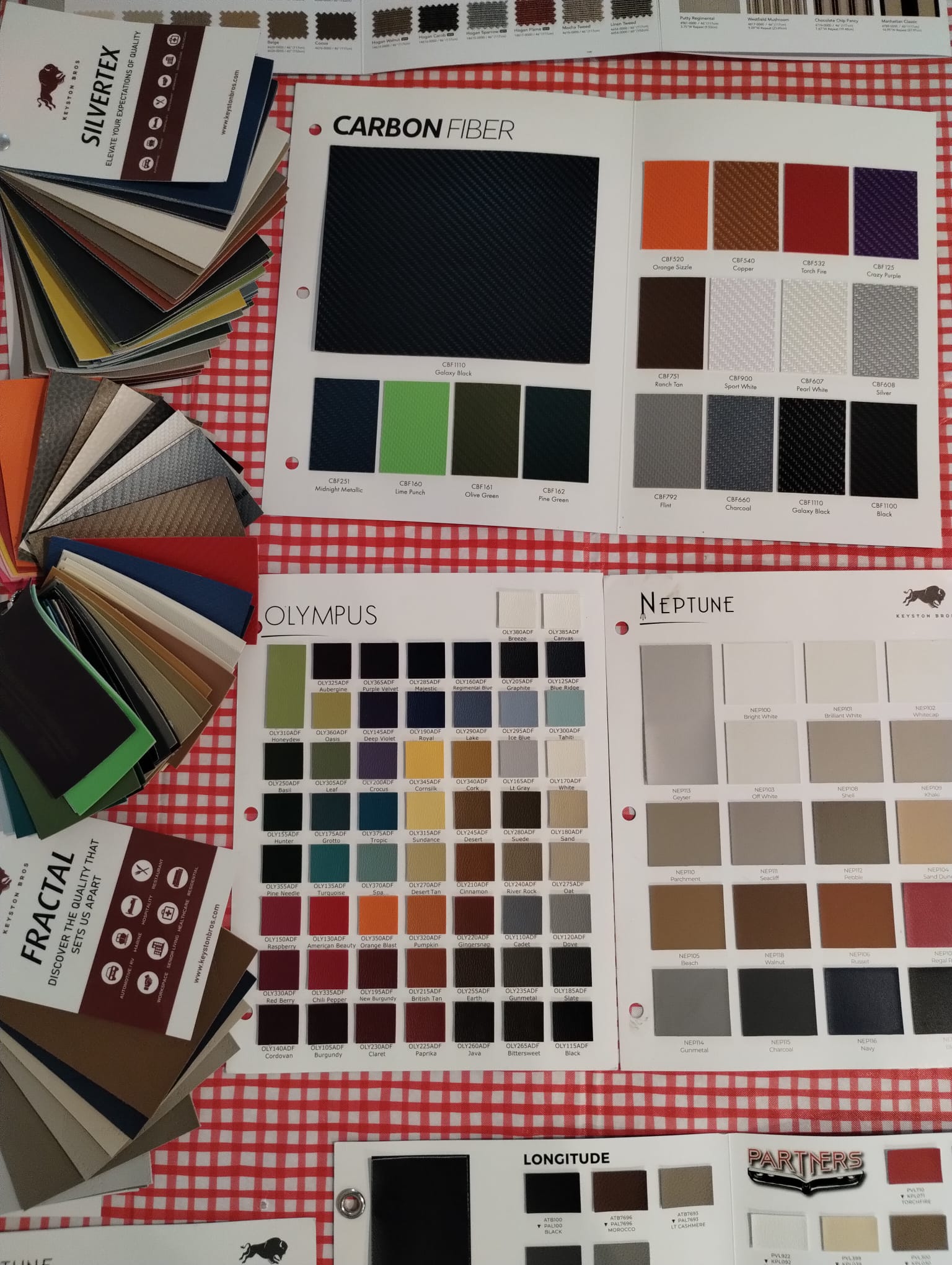 Fanned-out marine vinyl color swatch sample books, including Carbon Fiber, Olympus, and Neptune color charts, used for custom boat upholstery selection.