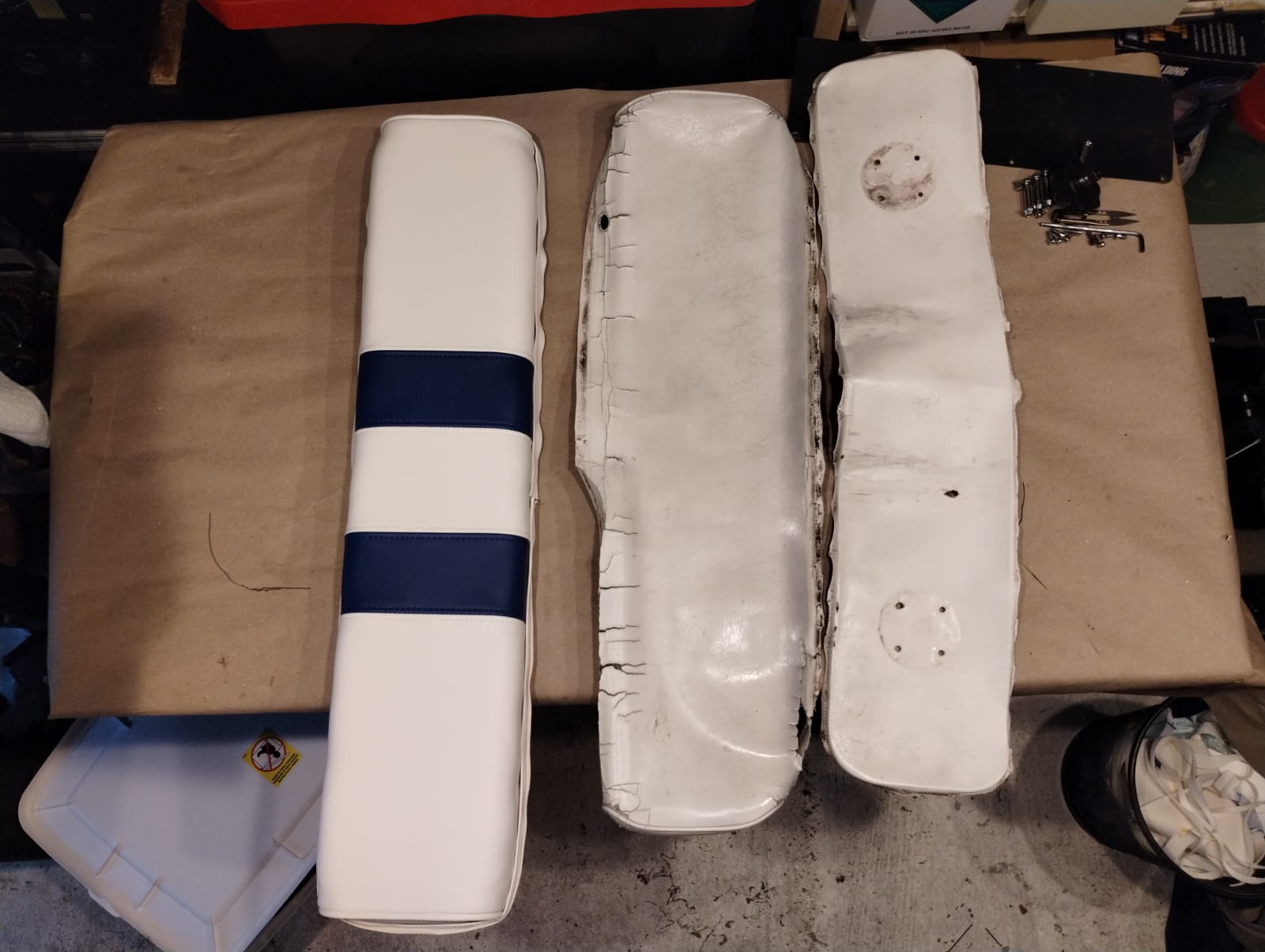 New white and navy boat cushion next to two worn, cracked original cushions before reupholstery